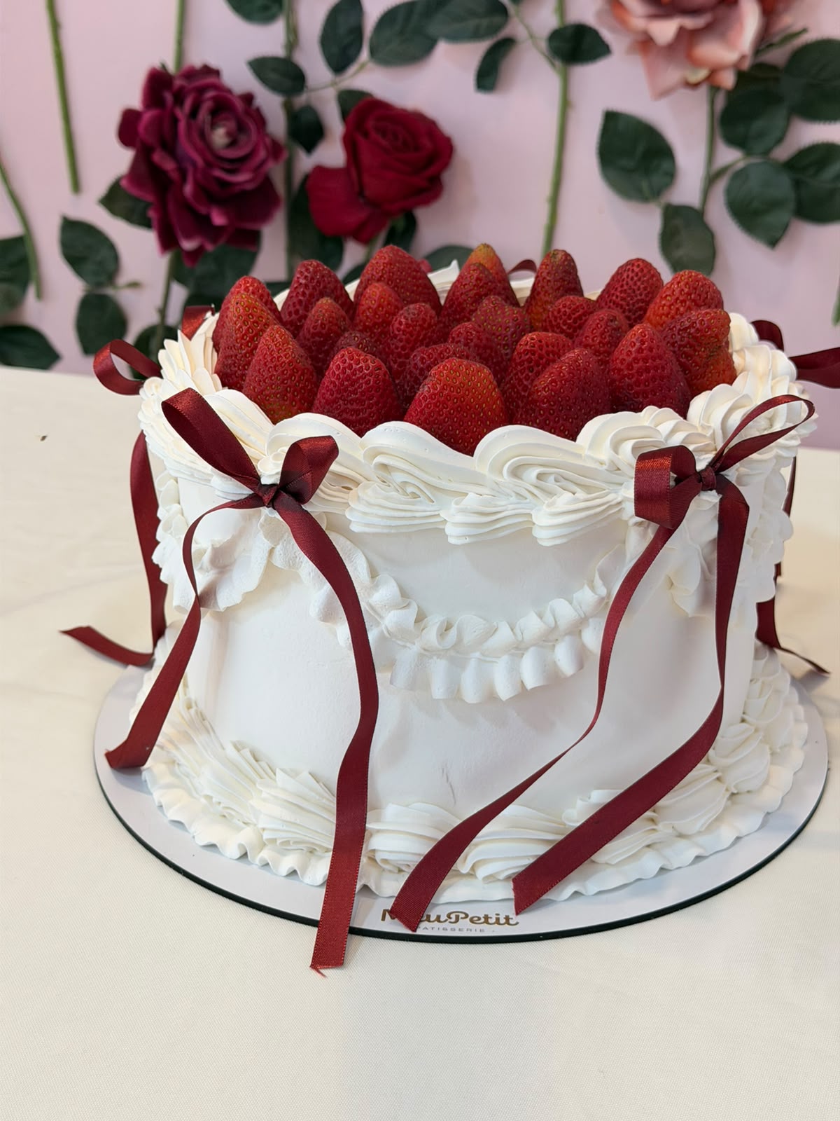 Bolo de morango com chantilly e laços de fita vinho sobre base da marca
